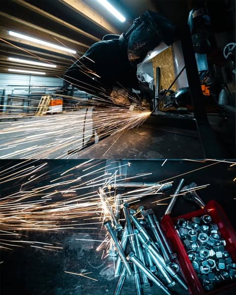Meulage d'une pièce métallique dans l'atelier, gerbe d'étincelles et visserie inox
